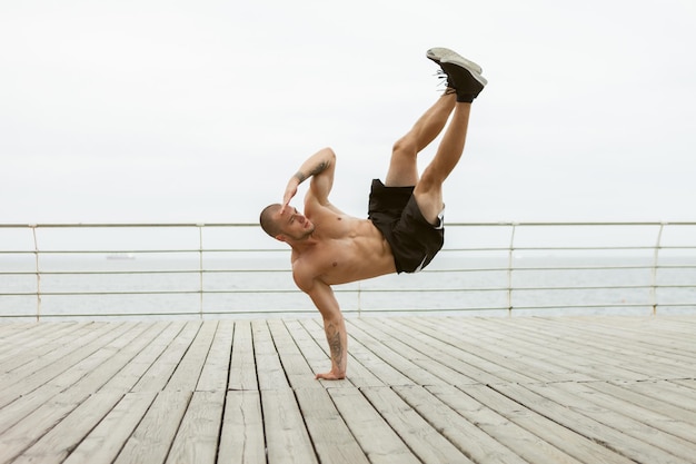 L'homme musclé de remise en forme de bodybuilder avec un torse nu se tient sur un bras sur la plage