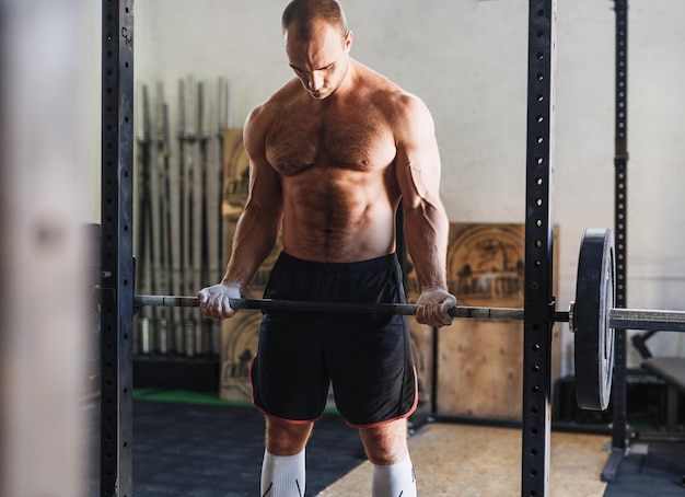 Un homme musclé sans chemise soulevant une barre pendant qu'il fait de l'exercice au gymnase