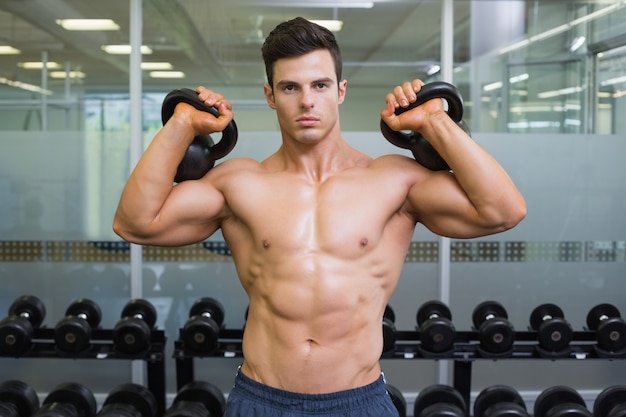 Homme musclé soulevant des cloches de la bouilloire dans la salle de gym