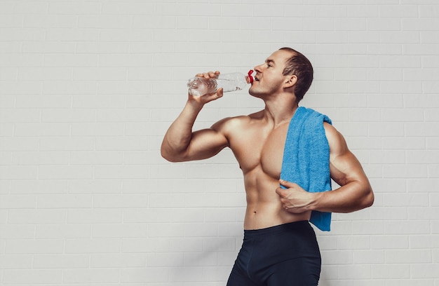Homme musclé tient une bouteille d'eau tout en portant des vêtements de sport avec une serviette isolé sur fond blanc