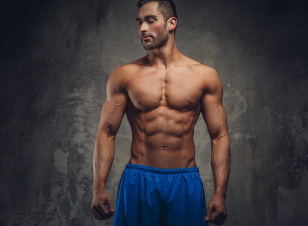 Homme musclé torse nu posant sur un fond gris.