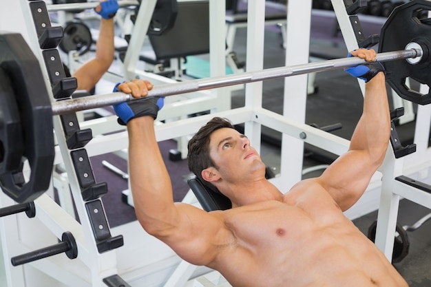 Homme musclé torse nu, soulevant des haltères dans la salle de gym