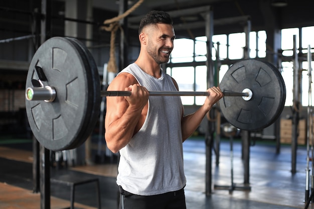 Homme musclé travaillant dans une salle de gym faisant des exercices avec haltères au biceps.