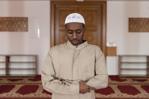 Homme musulman africain faisant la prière traditionnelle à Dieu tout en portant une casquette traditionnelle Dishdasha