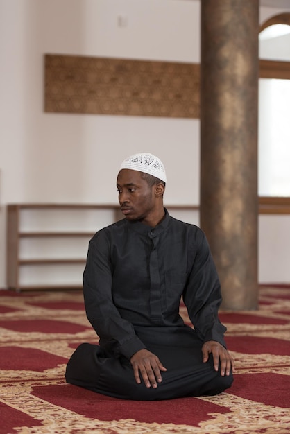 Homme musulman africain faisant la prière traditionnelle à Dieu tout en portant une casquette traditionnelle Dishdasha