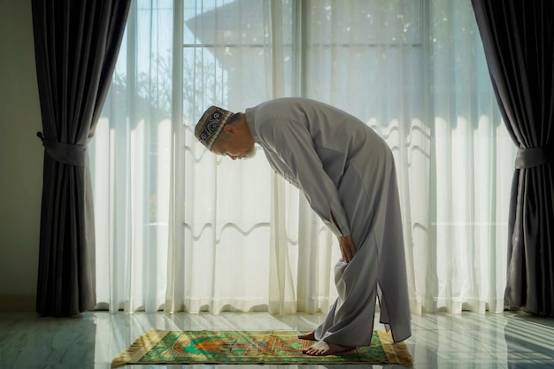 Un homme musulman âgé avec une barbe grise prie à la maison pendant la pandémie de coronavirus. Covid-19, concept de quarantaine