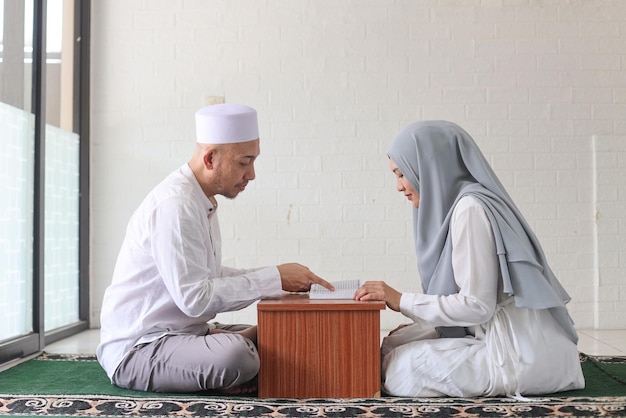 Homme musulman asiatique enseignant une femme lisant le Coran ou le Coran dans la mosquée