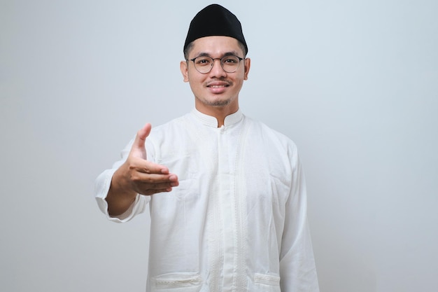 Homme musulman asiatique sur fond isolé souriant amical offrant une poignée de main comme salutation et accueil