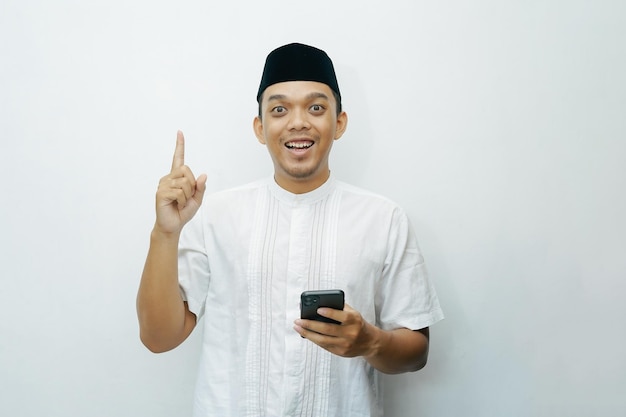 Photo un homme musulman asiatique indonésien souriant tenant un smartphone tout en montrant le doigt pointeur vers le haut