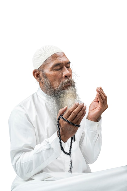 Homme musulman avec une barbe portant une casquette blanche priant avec des perles de prière sur ses mains