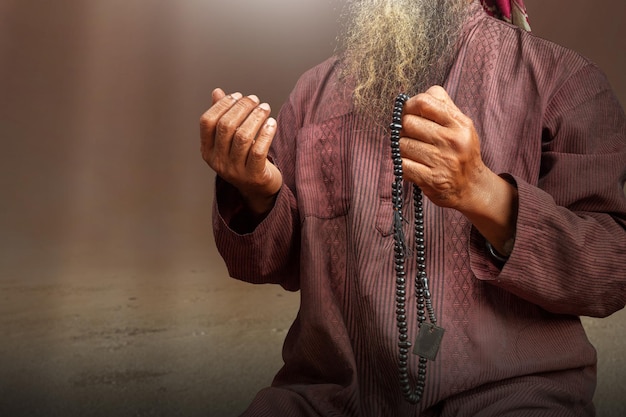 Homme musulman avec une barbe portant un keffieh avec agal priant avec des perles de prière sur ses mains