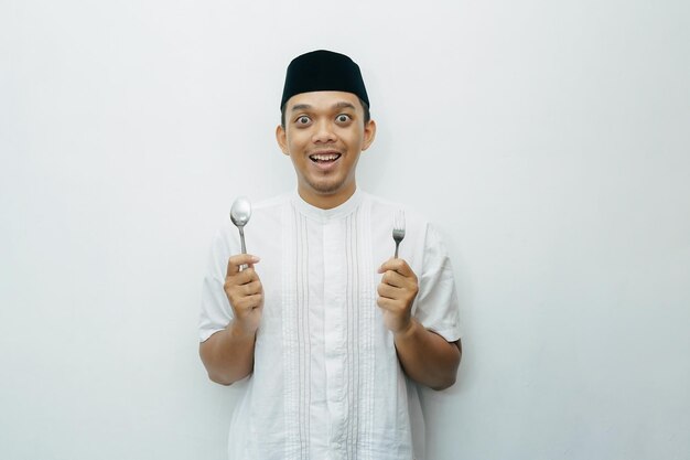 Photo un homme musulman indonésien asiatique excité tenant une cuillère et une fourchette dans les mains, prêt à manger.