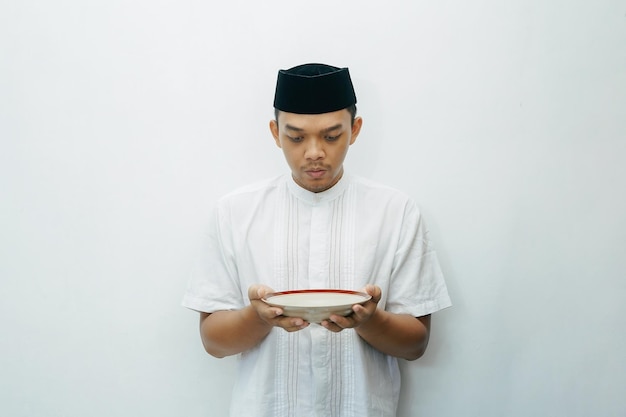 Photo un homme musulman indonésien asiatique tenant un plat vide et le regardant concept de jeûne du ramadan