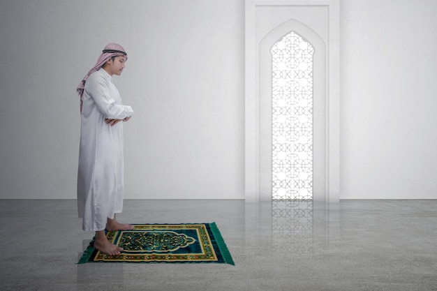 Homme musulman avec keffieh avec agal en position de prière salat sur le tapis de prière