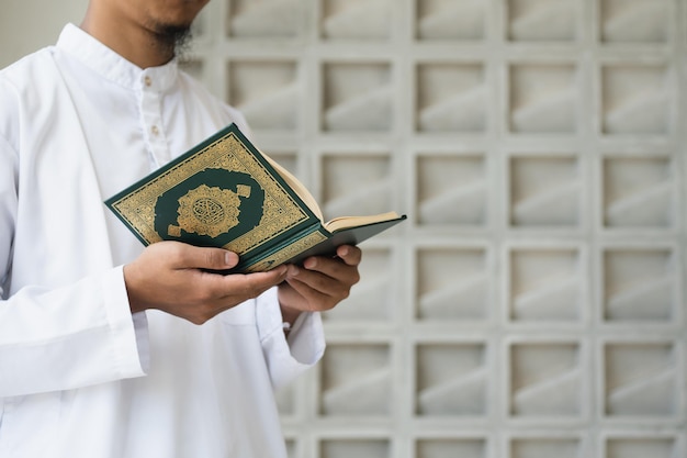 Photo homme musulman lisant le saint coran saint coran dans la main avec la signification du texte arabe de l'arrière-plan du concept islamique al quran