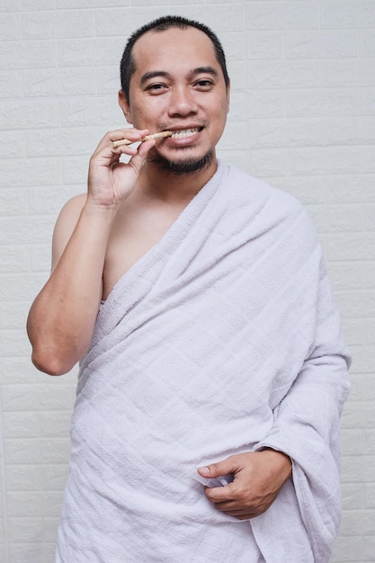 Homme musulman portant des vêtements blancs ihraam et tenant un siwak se nettoyant les dents