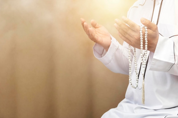 Homme musulman religieux priant à l'intérieur de la mosquéeLes hommes prient leur Dieu de l'IslamMettez la robe blanche pureTenez le collier de perles les mains à l'avant La foi en l'Islam