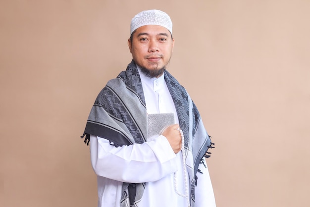 Un homme musulman religieux tenant le Coran devant sa poitrine sur un fond beige