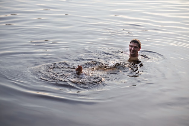 Homme nageant dans les eaux grises du lac, de la rivière ou de la mer par temps nuageux.