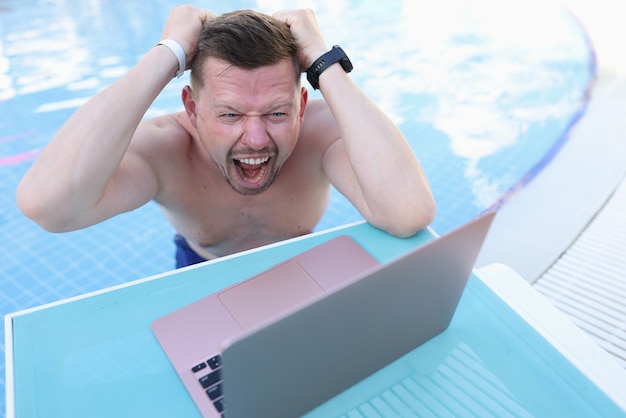Homme nageant dans la piscine et s'arrachant les cheveux devant un écran d'ordinateur portable
