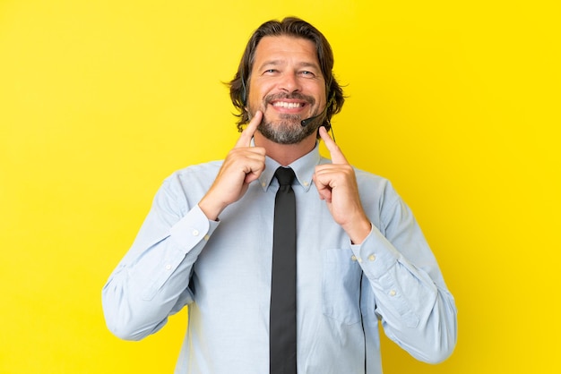 Homme néerlandais de télévendeur travaillant avec un casque isolé sur fond jaune souriant avec une expression heureuse et agréable