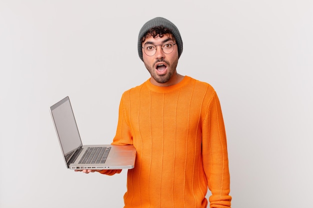 Homme nerd avec ordinateur à l'air très choqué ou surpris, regardant la bouche ouverte en disant wow