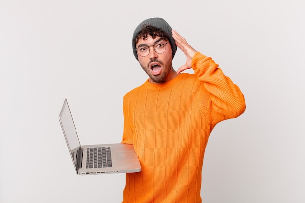 Homme nerd avec ordinateur criant avec les mains en l'air, se sentant furieux, frustré, stressé et contrarié