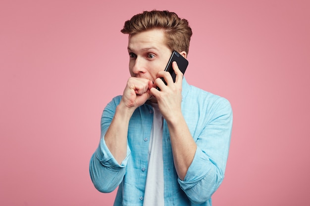 Un homme nerveux garde les poings dans la bouche pendant la conversation via un smartphone
