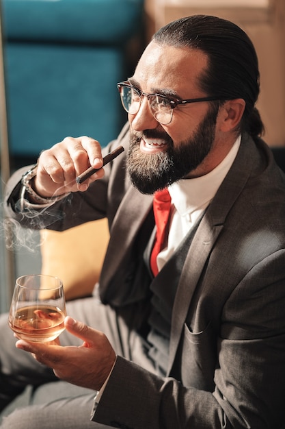 Homme nerveux. Épuisé nerveux homme aux cheveux noirs barbu fumant un cigare et regardant dans la fenêtre