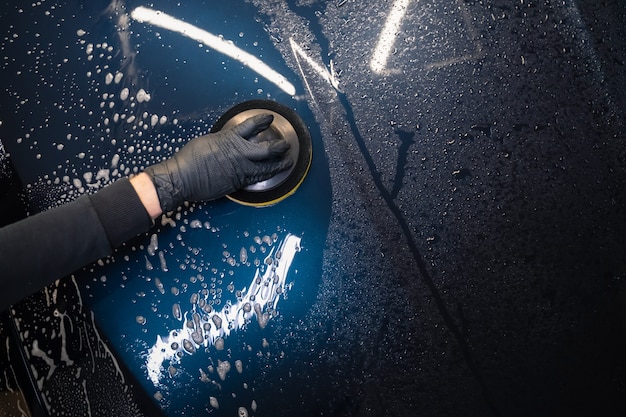 L'homme nettoie le capot de la voiture avec une éponge circulaire.