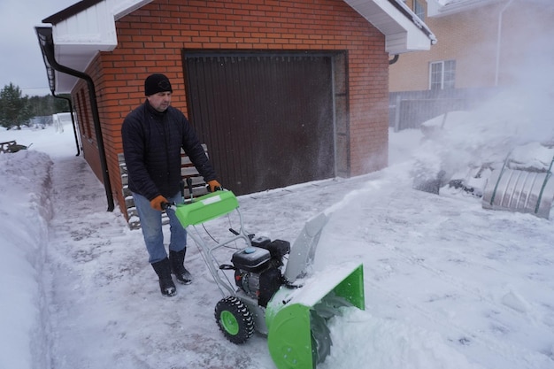 Un homme nettoie de la neige en hiver dans la cour de la maison un homme nettoie la neige avec un souffleur de neige