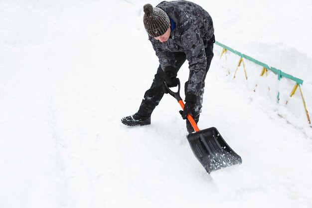 Un homme nettoie la neige avec une pelle en hiver dans une cour balayée après une chute de neige. Conditions météorologiques hivernales, pelle à neige pour coffre de voiture