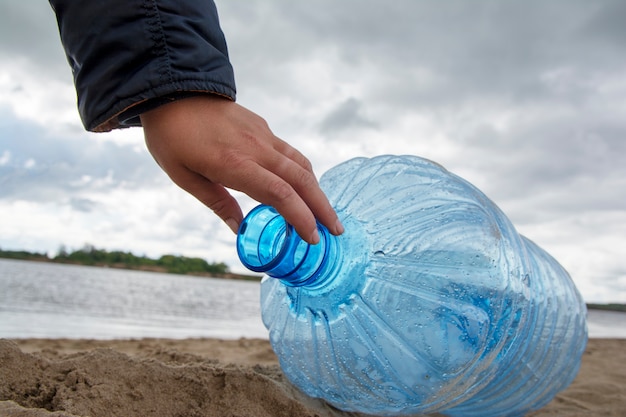 Un homme nettoie les ordures et les bouteilles en plastique sur une plage sale en les ramassant. Pollution environnementale