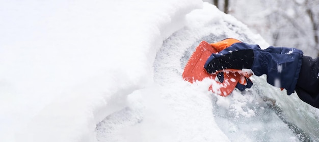 L'homme nettoie sa voiture après une chute de neige Nettoyer la neige du pare-brise Gratter la glace Nettoyage des vitres de voiture en hiver