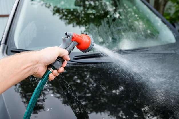 Un homme nettoie sa voiture dans un lave-auto, une brosse laissant des traces de shampooing