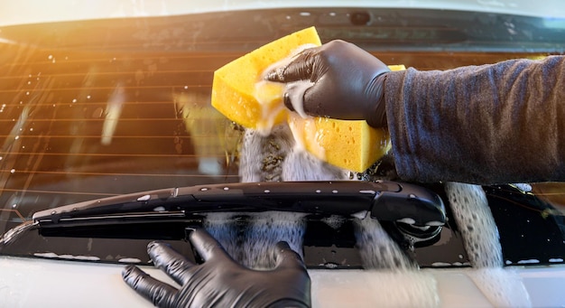 Un homme nettoie sa voiture avec une éponge et du liquide de lavage. Lavage de voiture dans le garage à la maison.