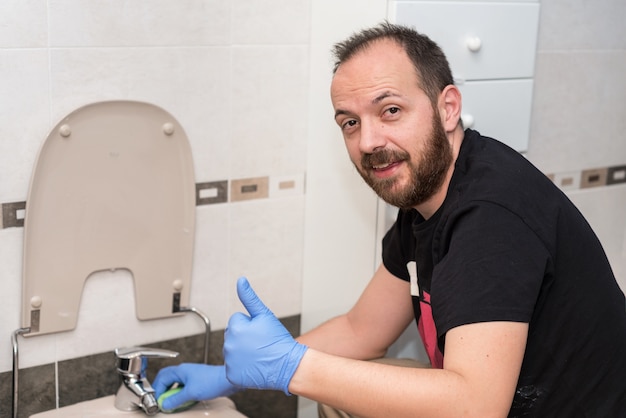 Homme nettoyant la cuvette des toilettes. Émotion positive montrant les pouces vers le haut.