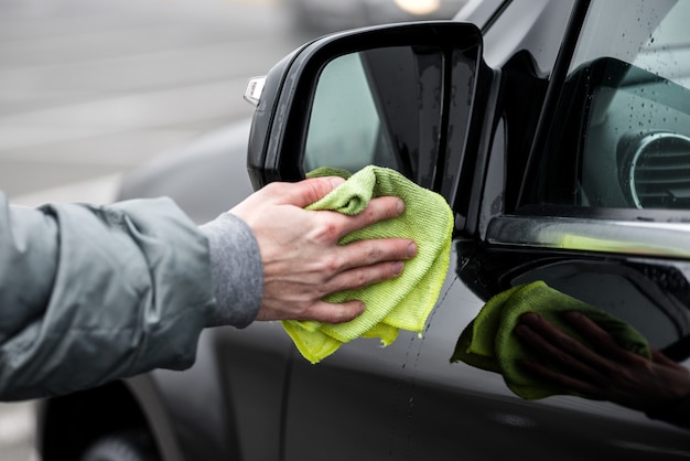 Un homme nettoyant le rétroviseur gauche de la voiture avec un chiffon en microfibre, concept de détail de voiture.