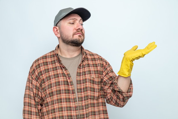 Homme nettoyeur slave confus avec des gants en caoutchouc regardant sa main