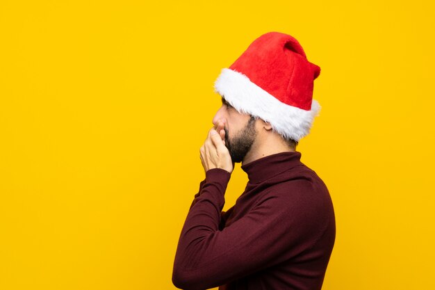 Homme, à, noël chapeau, sur, isolé, mur jaune, couvrir bouche, et, regarder, côté