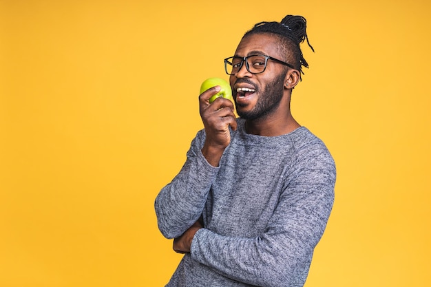 Homme noir afro-américain en bonne santé tenant une pomme isolée sur fond jaune. Concept de régime alimentaire sain.