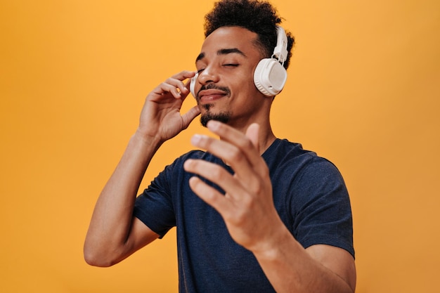 Homme noir appréciant la musique avec des écouteurs Gars heureux en t-shirt élégant écoutant des chansons sur fond isolé orange