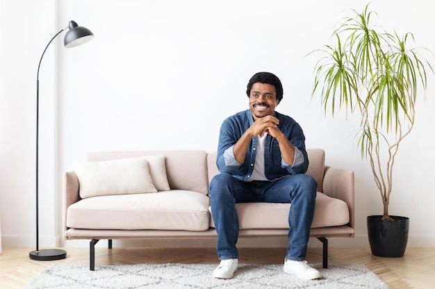 Un homme noir assis sur le canapé dans le salon et souriant.