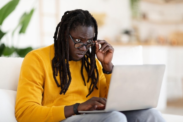 Homme noir confus regardant l'écran d'ordinateur portable tout en utilisant l'ordinateur à la maison