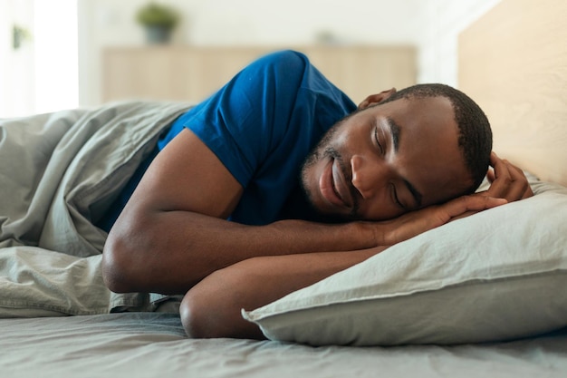 Homme noir du millénaire dormant appréciant le repos allongé dans une chambre moderne