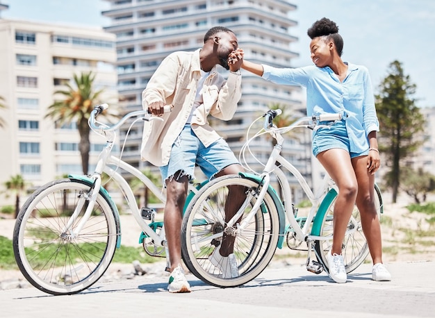 Homme noir embrasse la main d'une femme et des vacances dans un parc en plein air à Miami Couple sur un rendez-vous d'été romantique à vélo dans la rue de la ville et une petite amie heureuse