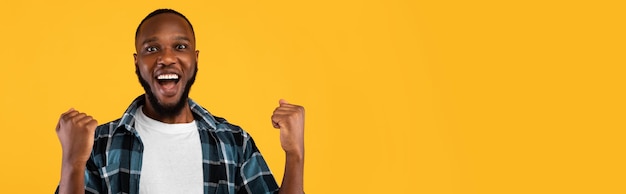 Homme noir excité serrant les poings posant sur le panorama de fond jaune