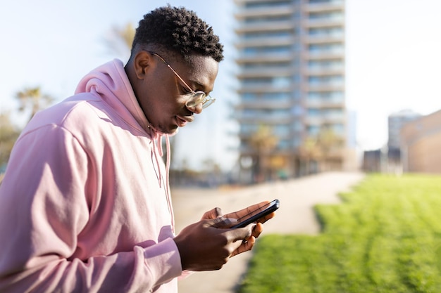 Homme noir à l'extérieur utilisant un téléphone portable pour envoyer un message texte Copier l'espace