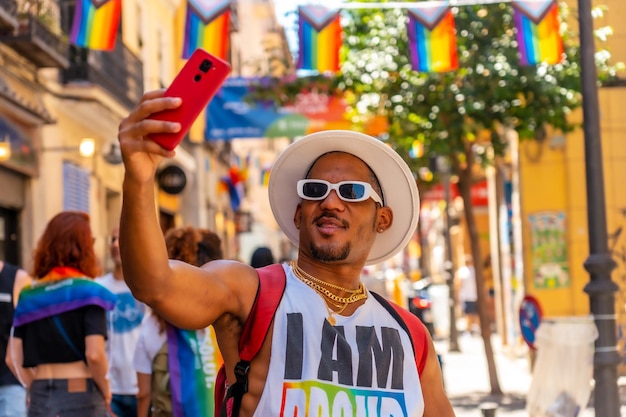 Un homme noir gay à la fête de la fierté prenant un selfie avec le drapeau LGBT du téléphone