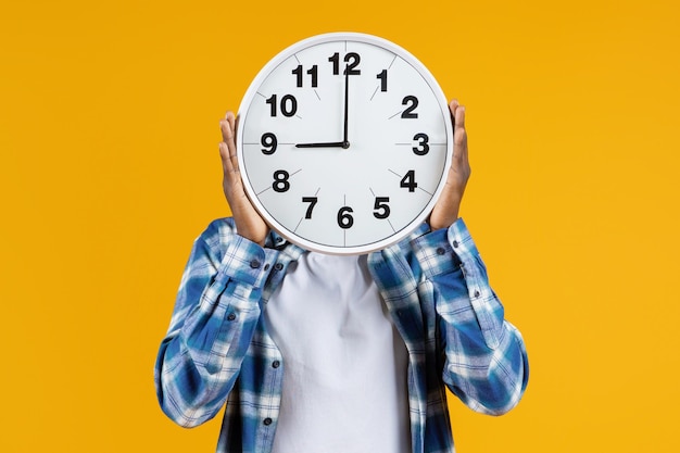 Un homme noir méconnaissable tenant une grande horloge ronde devant son visage.
